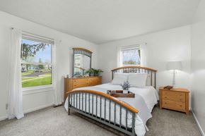 Fort Wayne apartment for rent - A bedroom with a large bed, a window with a view of a street, and a nightstand with a lamp.