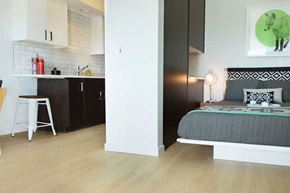 Portland apartment for rent - A modern bedroom with a grey bed and a kitchen area with black cabinets.