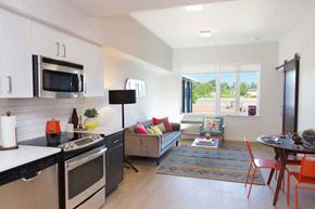Portland apartment for rent - A modern kitchen with a black stove top oven and microwave, a dining table with chairs, and a couch with colorful pillows.