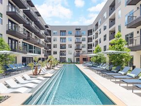 San Antonio apartment for rent - A long rectangular pool in the middle of a courtyard surrounded by lounge chairs and umbrellas.