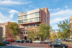Ithaca apartment for rent - A modern building with a glass facade is situated on a street with cars parked on the side.