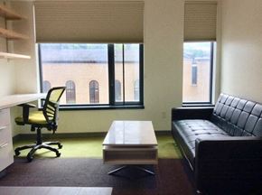 Ithaca apartment for rent - A black leather couch sits in front of a window in a room with a desk and a chair.