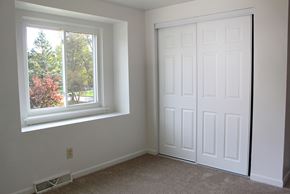 Amherst triplex for rent - A room with a white door and a window with a view of trees and flowers.