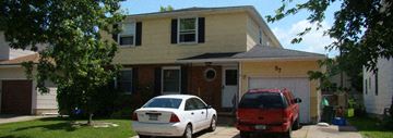 Depew triplex for rent - A white car is parked in front of a yellow house.