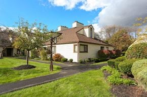 East Amherst condo for rent - A house with a brown roof and white walls is surrounded by a well-manicured lawn and a clear sky.