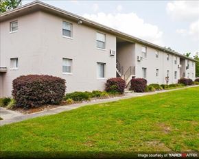 Gainesville apartment for rent - a white building with a green lawn and bushes