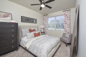 Charlotte apartment for rent - Cozy bedroom interior featuring a bed with layered bedding, accent chair, and wall art, with natural light coming through a window.
