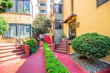 Oakland apartment for rent - A red pathway leads to a building with a tree and bushes on either side.