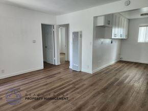 Lomita apartment for rent - A spacious room with wooden flooring and white walls, with a logo for Beach Front Property Management in the bottom left corner.