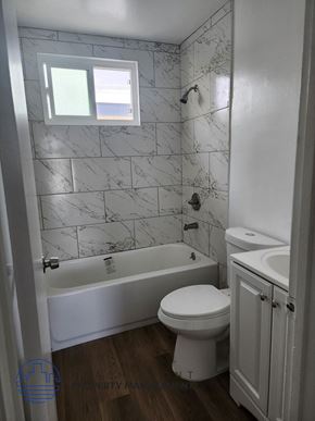 Lomita apartment for rent - A white toilet sits in a bathroom with a marble tile wall and a white bathtub.
