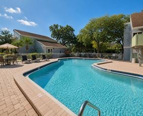 Tampa apartment for rent - A swimming pool surrounded by a brick patio and a white building in the background.