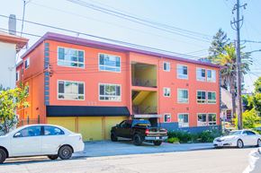 Oakland apartment for rent - A bright orange building with a white car parked in front.