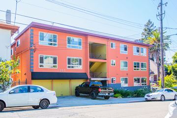 Oakland apartment for rent - A bright orange building with a white car parked in front.
