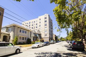 Oakland apartment for rent - A street view with cars parked on the side and apartment buildings in the background.
