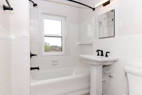 Minneapolis apartment for rent - A white bathroom with a tub, sink, and mirror.
