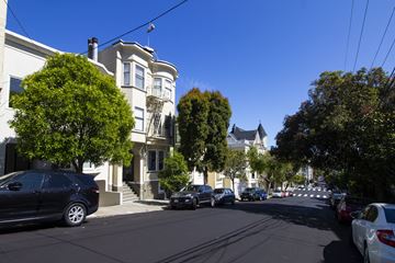 San Francisco apartment for rent - A street view with cars parked on the side and a white building with a tower in the background.