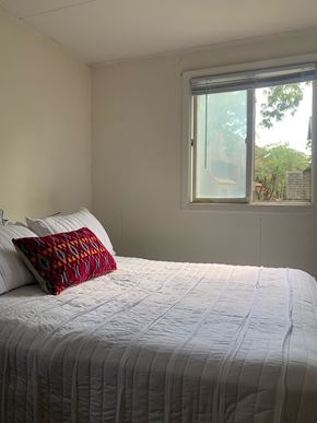 Ithaca apartment for rent - A bed with a white comforter and a red and black pillow is in front of a window.