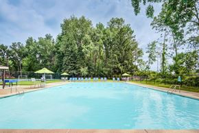 Tonawanda apartment for rent - A large outdoor swimming pool surrounded by trees and a fence.