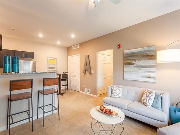 Canonsburg apartment for rent - A living room with a grey couch, a bar area with stools, and a painting on the wall.