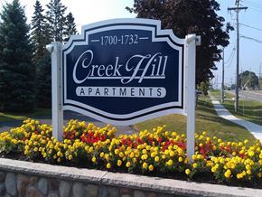 Webster apartment for rent - A sign for Creek Hall Apartments is surrounded by flowers.