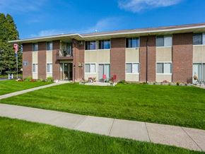 Webster apartment for rent - A building with a flag on the left side and a small garden in front.