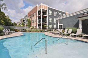 Dayton apartment for rent - A swimming pool in front of a building with a fence and trees.