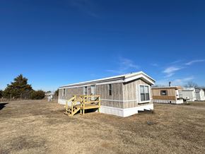 Shawnee house for rent - A wooden house with a porch is in the foreground of a grassy field.