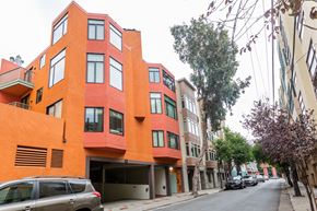San Francisco apartment for rent - A street view of a red building with a car parked in front.
