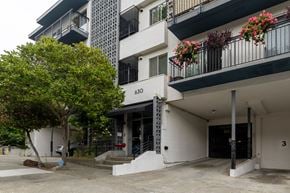 Oakland apartment for rent - A white building with a black awning and a tree in front of it.