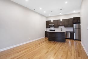 Chicago apartment for rent - an empty living room and kitchen with wood flooring and stainless steel appliances