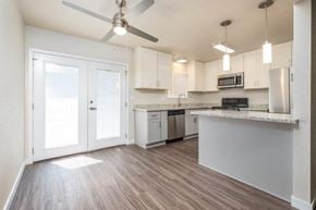 Manteca apartment for rent - View of open kitchen with wood look flooring, stone counters, white cabinets, stainless appliances, ceiling fan, and lighting