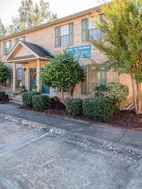 Maumelle apartment for rent - the front of a brick building with a blue sign and trees and bushes