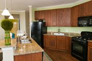 Frederick apartment for rent - kitchen at VistaView apartments in Frederick, MD with black appliances, dark wood cabinets and flooring, kitchen island with sink and counter seating and stone countertops at VistaView, Frederick