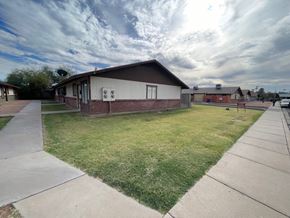 Mesa apartment for rent - A small building with a brown roof and a white wall with a red door is surrounded by a grassy area and a concrete walkway.
