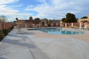 Mesa apartment for rent - A large outdoor swimming pool surrounded by a concrete patio and a red brick wall.