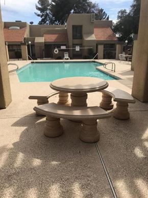 Mesa apartment for rent - A concrete table and chairs are in the foreground of a pool area.