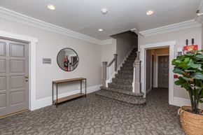 San Francisco apartment for rent - A hallway with a grey carpet, a mirror, a bench, and a staircase.