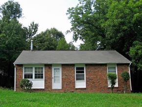 Greensboro house for rent - A small house with a white door and windows surrounded by greenery.