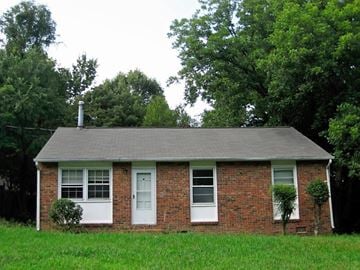 Greensboro house for rent - A small house with a white door and windows surrounded by greenery.