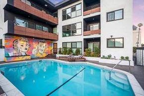 West Hollywood apartment for rent - A mural of two people is on the side of a building next to a pool.