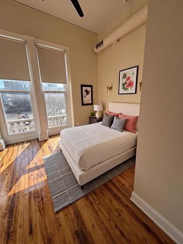 Louisville apartment for rent - A bedroom with a bed, pillows, a lamp, and a window with blinds.