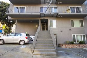 San Francisco apartment for rent - A silver car is parked in front of a two-story building with a staircase leading to the entrance.