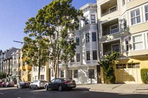 San Francisco apartment for rent - A street view of a row of apartment buildings with cars parked on the side of the road.