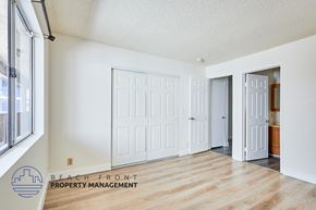 Long Beach apartment for rent - A room with white walls and wooden floors, featuring a white door and a window with a view of buildings outside.