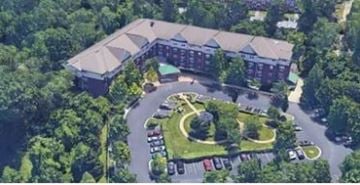 Gwynn Oak apartment for rent - A large building surrounded by trees with a parking lot in front.