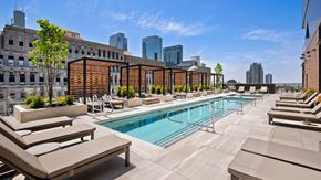 Chicago apartment for rent - Looking across the outdoor pool at Hubbard221. Lounge chairs go off to the left and right. Pergolas are across the pool with more lounge chairs beneath them. City buildings are seen rising in the back