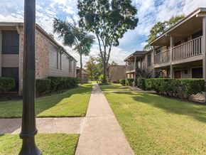 Houston apartment for rent - a walkway between two apartment buildings with grass and trees