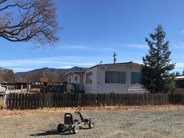 Hayfork house for rent - A lawn mower is in the foreground of a residential area with a house and a fence.