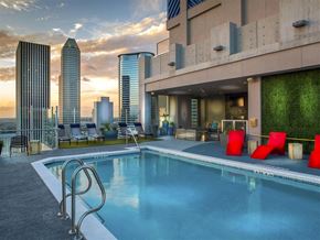 Houston apartment for rent - A swimming pool is surrounded by a red chair and a building with a green wall.