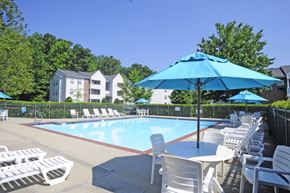 Hampton apartment for rent - A pool area with chairs and umbrellas is surrounded by a fence and houses.